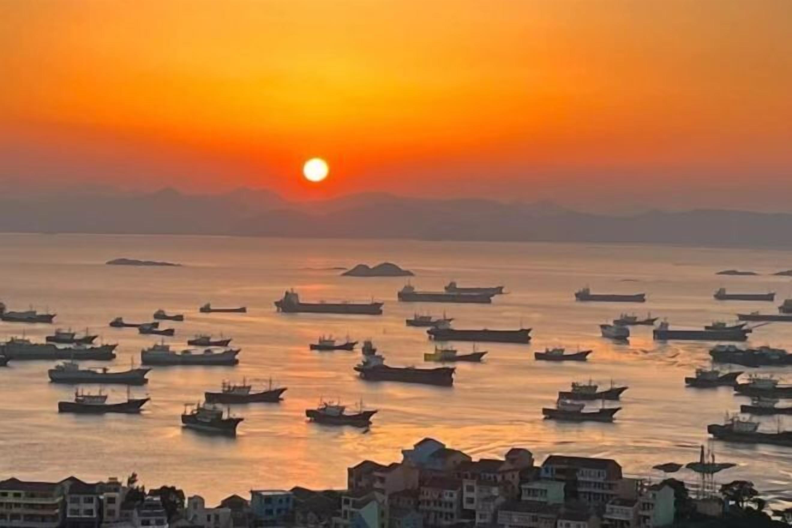 A coastal scene with numerous boats at sunset.