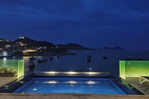 Una piscina con vista al mar y colinas distantes.