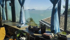 A room with a view of the sea, a window with blue curtains, and a table with books and plants. - Between sky and sea (Wenling)