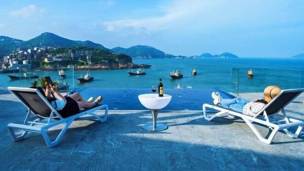 A terrace with lounge chairs overlooking a coastal view with boats and buildings. - Between sky and sea (Wenling)