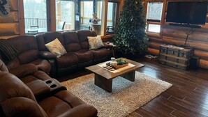 A cozy log cabin interior with a leather sofa, a coffee table, a Christmas tree, and a television. - The Southview Lodge. (Valemount)