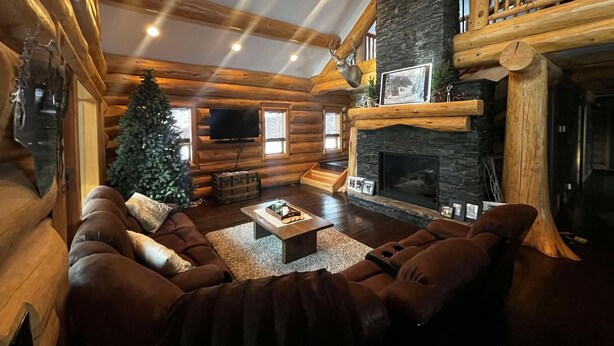 A log cabin interior with a fireplace, a Christmas tree, and a cozy seating area. - The Southview Lodge. (Valemount)