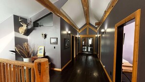 A hallway with dark wooden floors, wooden beams on the ceiling, and a wooden railing. - The Southview Lodge. (Valemount)