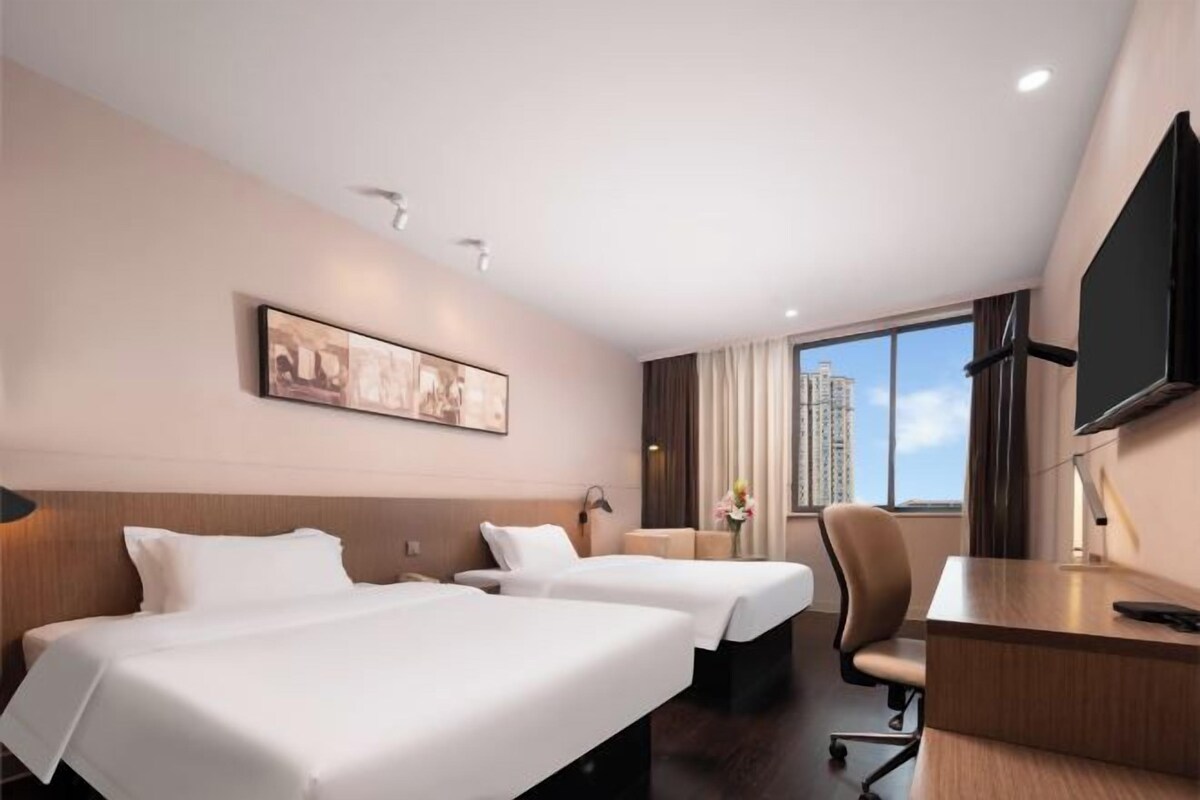 A hotel room with two beds, a desk, a chair, a TV, and a window with a city view.