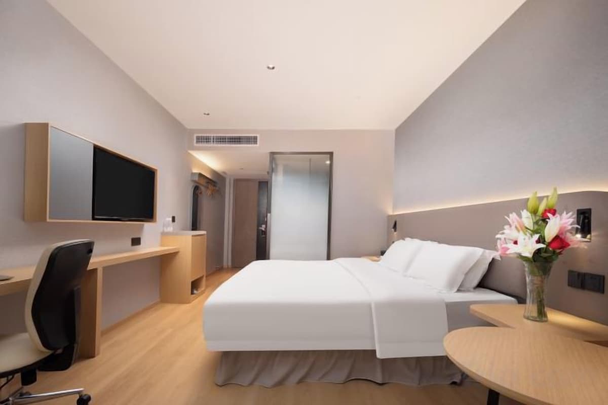 Una habitación de hotel con cama, escritorio, silla, televisión y un jarrón con flores.