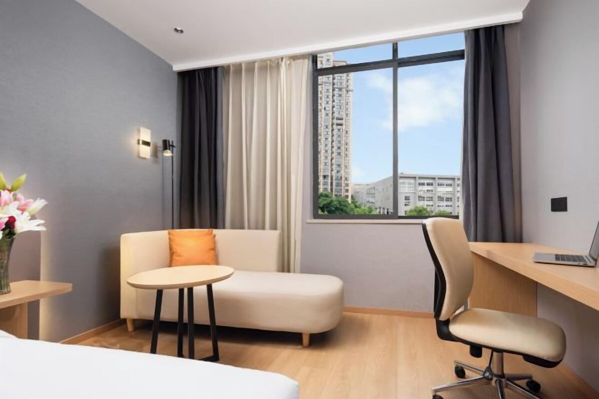 A hotel room with a bed, a sofa, a desk with a laptop, a chair, a small table, and a window with curtains.