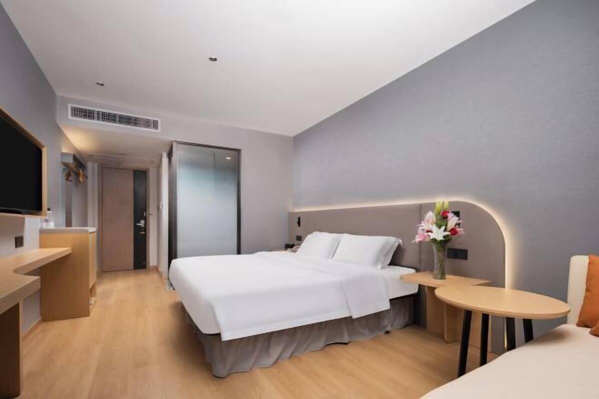 A modern hotel room with a bed, bedside table, and a small round table with a lamp.