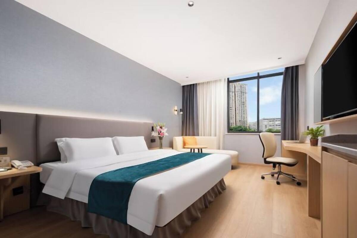 A hotel room with a large bed, a desk, a chair, and a TV.
