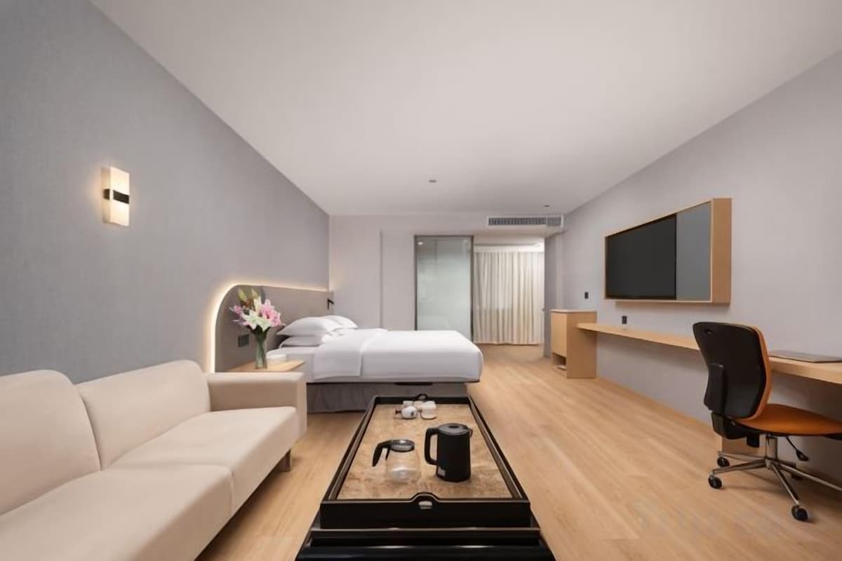 Una habitación de hotel moderna con cama, sofá, escritorio, televisor y mesa de centro.