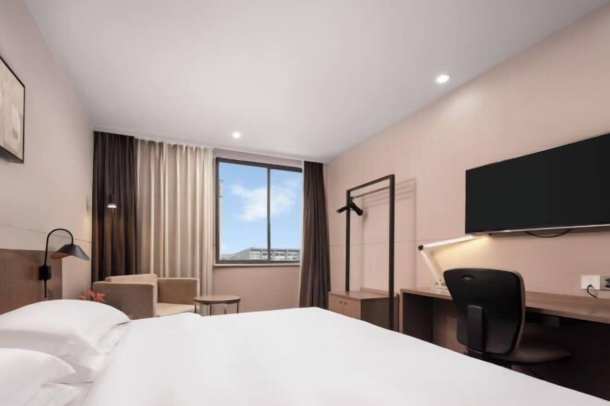 A hotel room with a bed, a desk, a chair, a TV, and a window with curtains.