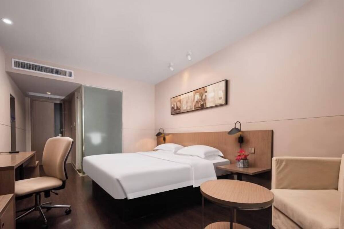 A hotel room with a bed, a desk, a chair, a round table, and a painting on the wall.