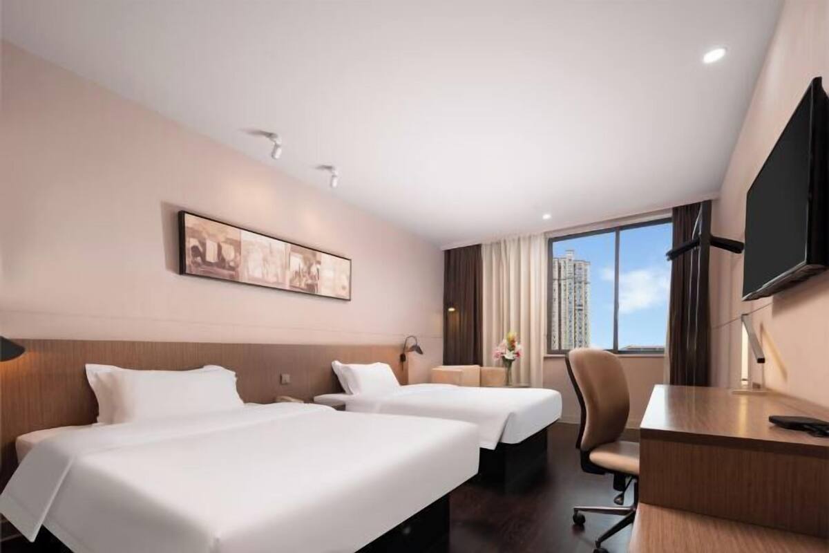 A hotel room with two beds, a desk, a chair, a TV, and a window with a city view.