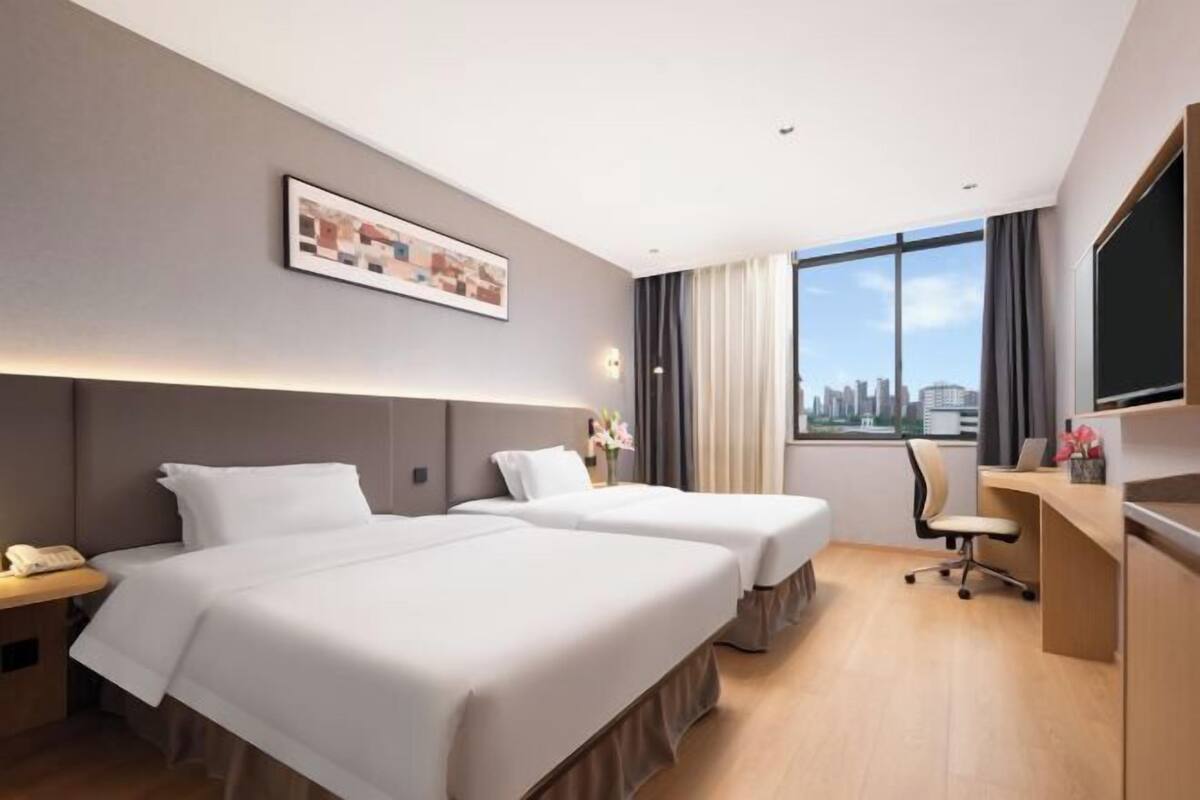 A hotel room with two beds, a desk, a chair, a phone, and a large window with a city view.