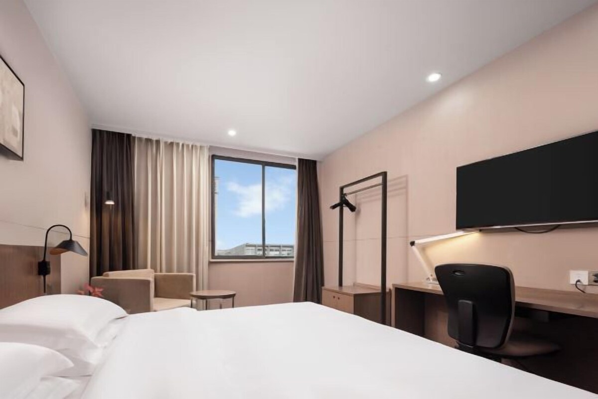 A hotel room with a bed, a desk, a chair, a TV, and a window with curtains.