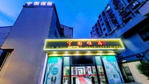 A hotel entrance with a neon sign, a red carpet, and a modern building facade. - Ningyuan Homestay (Zhoushan)