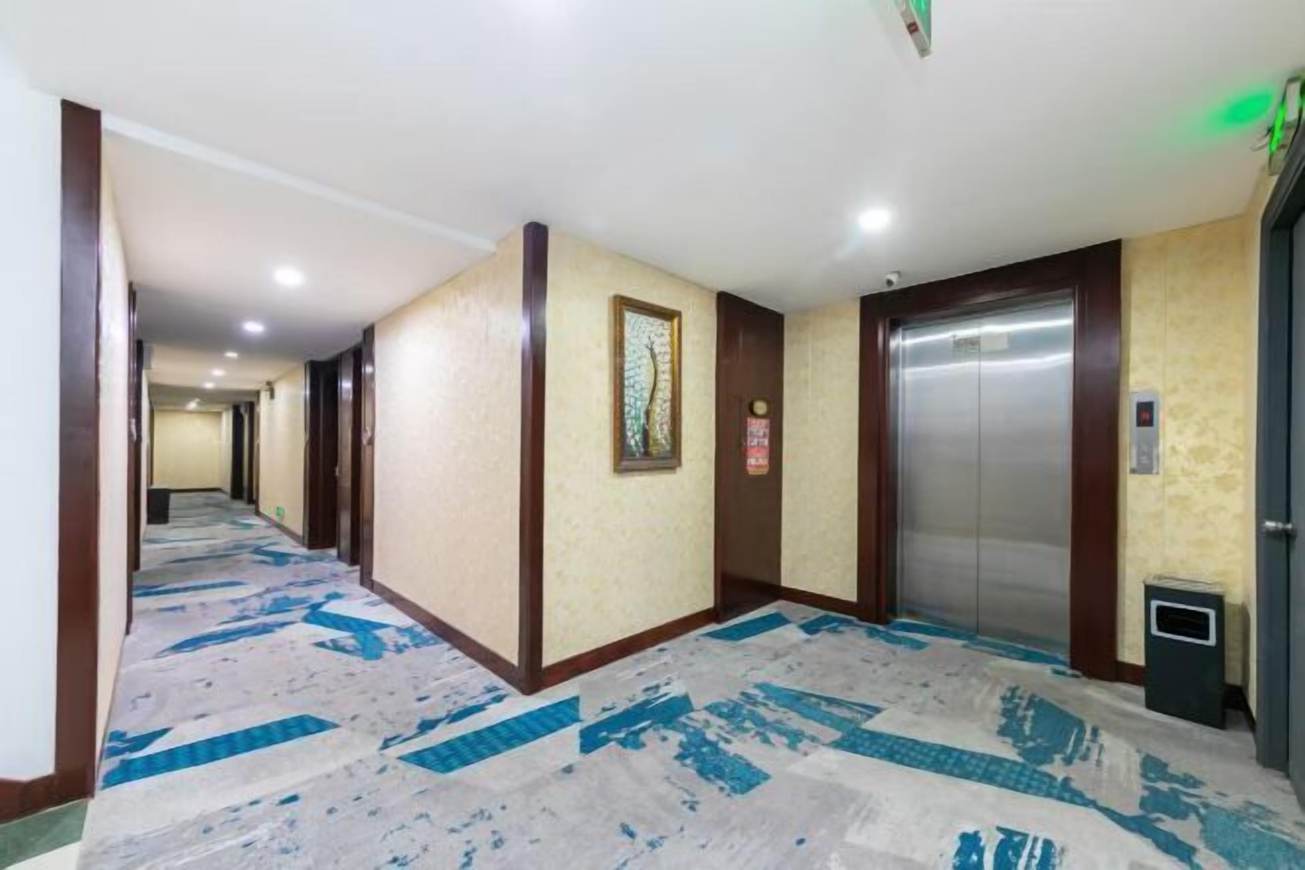 A hotel corridor with a patterned carpet, wooden doors, and an elevator.