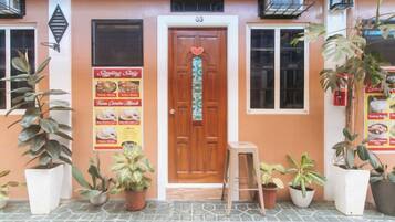 L'ingresso di un edificio con una porta in legno, piante in vaso e un cartellone con il menù.