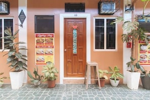 A building entrance with a wooden door, potted plants, and a menu poster. - RedDoorz @ Queens Hometel (Tagum)