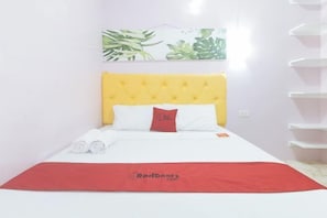 Cama bem arrumada com cabeceira amarela, roupa de cama branca e manta vermelha com texto.