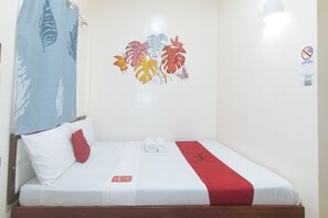 A single bed with white bedding and a red accent, a wall with a tropical leaf mural, and a no-smoking sign. - RedDoorz @ Queens Hometel (Tagum)