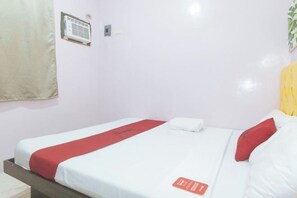 A single bed with a red and white bedspread, a white pillow, and a red pillow on a white wall with a small air conditioning unit and a light switch. - RedDoorz @ Queens Hometel (Tagum)