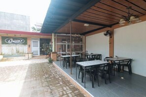 An outdoor patio area with tables and chairs, a covered seating area, and a building entrance with a sign. - RedDoorz @ Queens Hometel (Tagum)