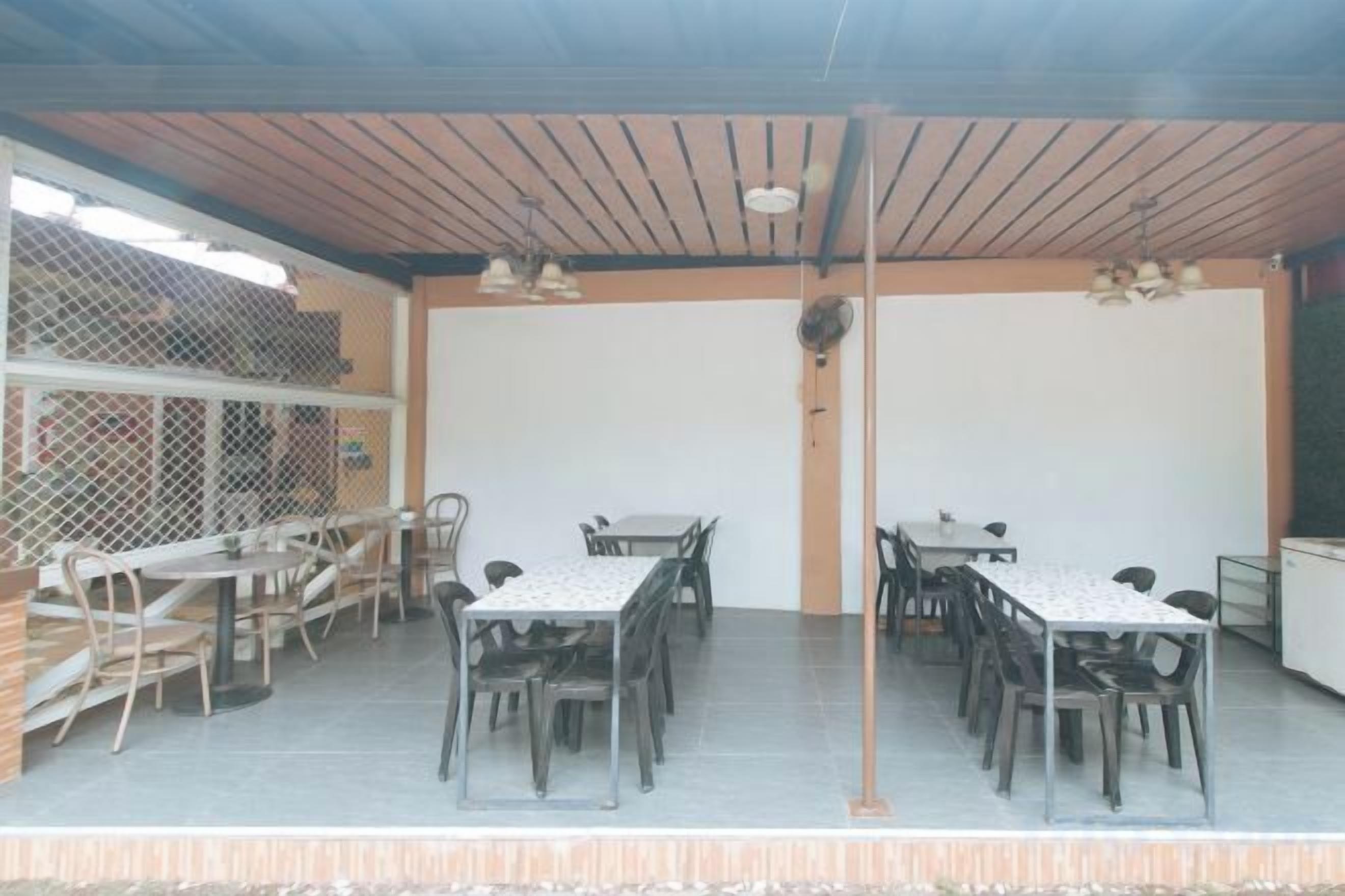 Un'area pranzo all'aperto riparata, con diversi tavoli e sedie, una ventola a soffitto e vista sull'esterno.