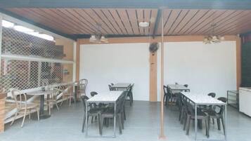 Un'area pranzo all'aperto riparata, con diversi tavoli e sedie, una ventola a soffitto e vista sull'esterno.