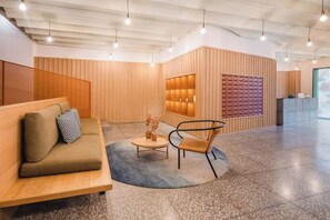 Un hall d’entrée moderne avec un comptoir d’accueil en bois, un espace détente avec un canapé et des fauteuils, et un sol à motifs.