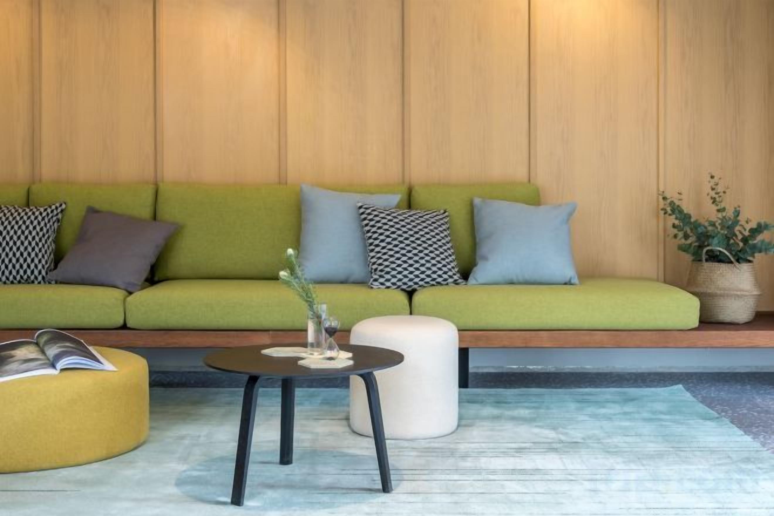 A green sofa with patterned cushions, a round coffee table, and a potted plant.