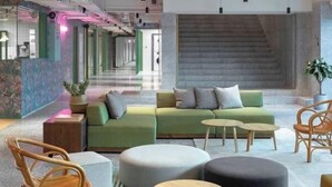 En modern entréhall med en grön soffgrupp, runda sittpallar och trästolar.