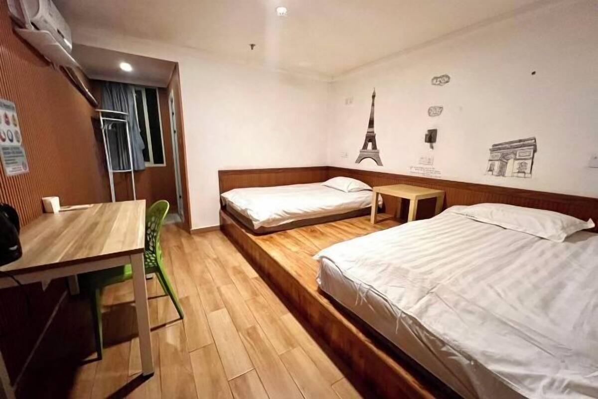 Een hotelkamer met een houten vloer, een bureau, twee enkele bedden en een stoel.