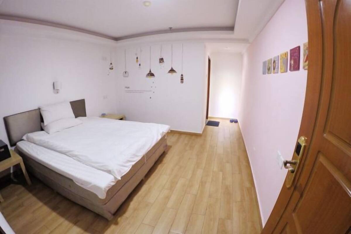 Een slaapkamer met een bed, nachtkastje, wandlampen en een deur met een handgreep.