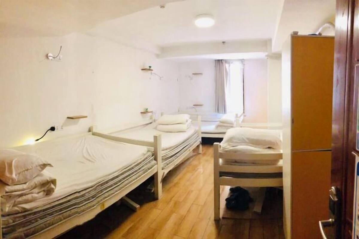 Een hotelkamer met drie enkele bedden, een houten garderobe en een klein tafeltje.