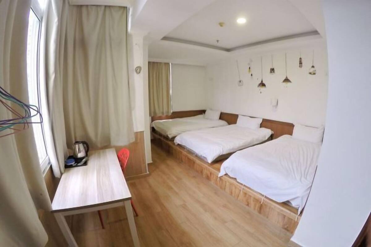 Hotelkamer met houten vloer, twee bedden, een klein tafeltje en een raam met gordijnen.