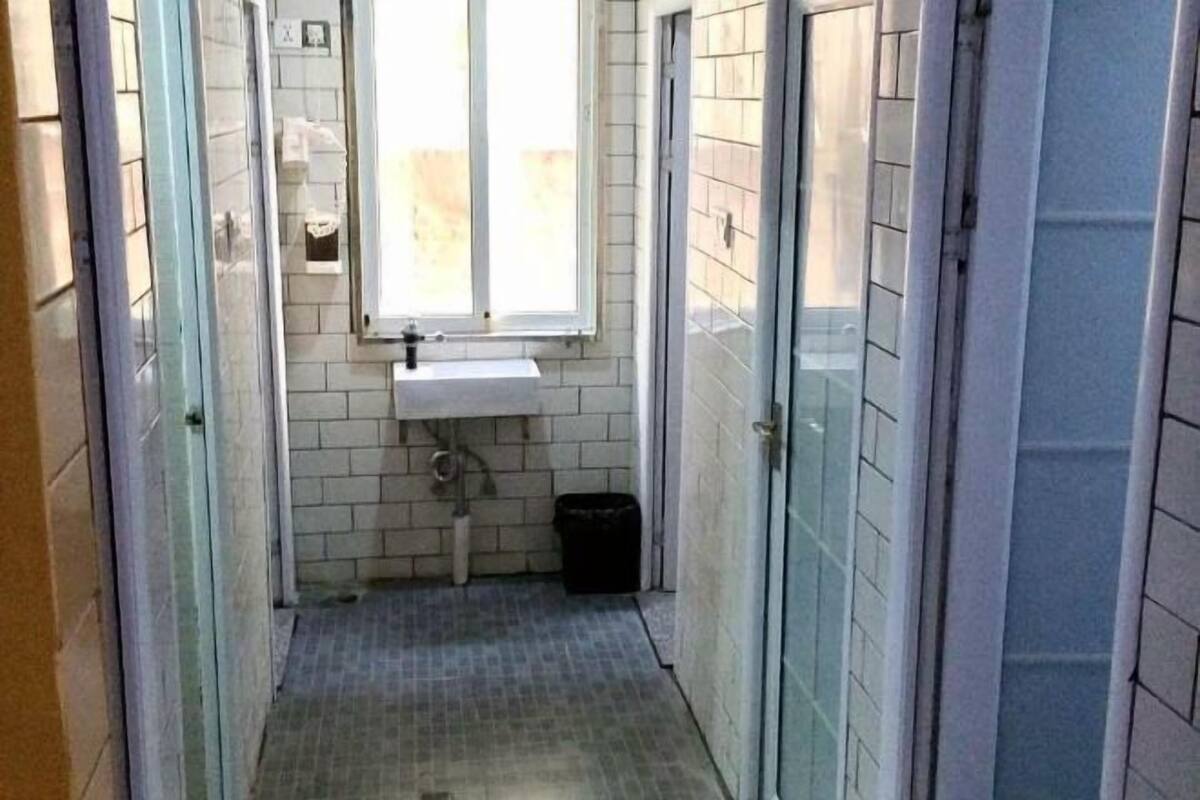 Een kleine badkamer met raam, wastafel en prullenbak.