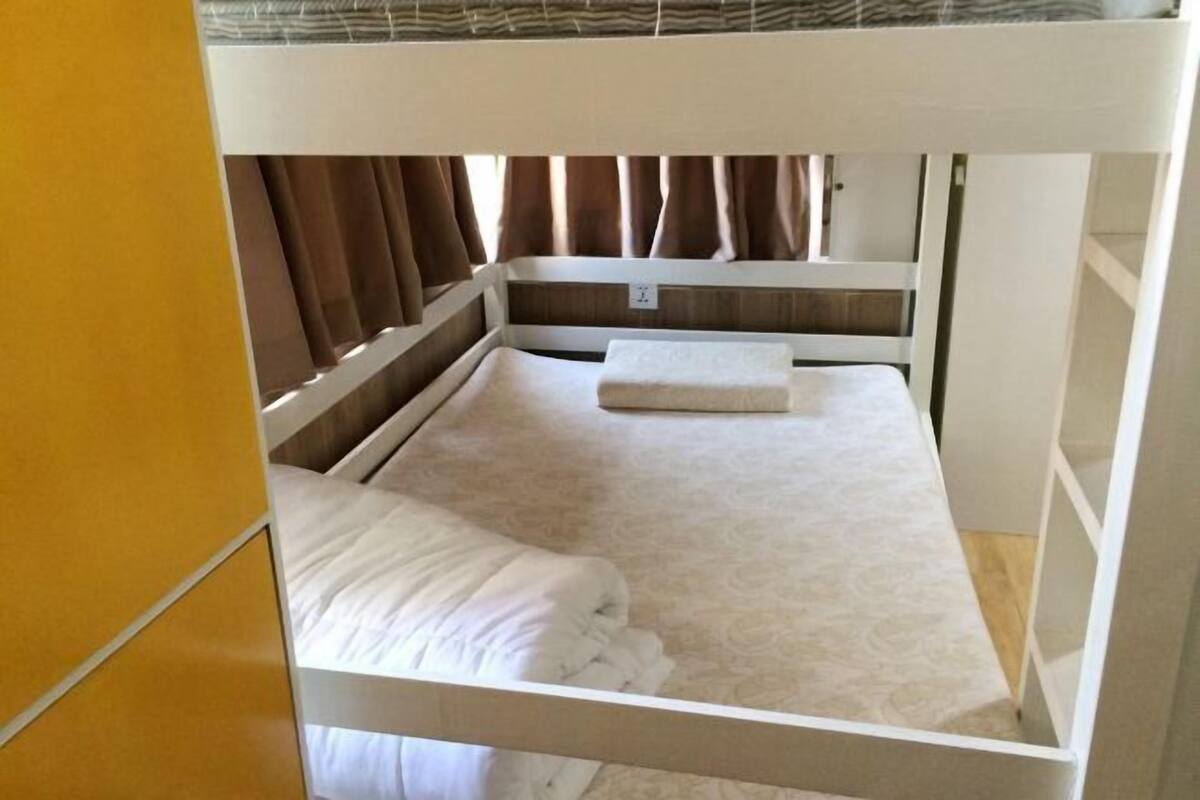Een stapelbed met matras en kussens, een nachtkastje en gordijnen.