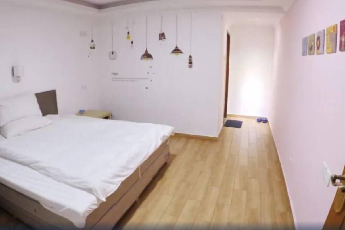 Een slaapkamer met een bed, houten vloer, witte muren en een deur naar een andere kamer.