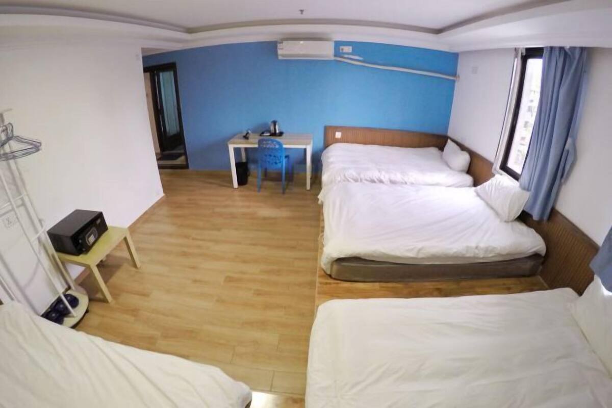Een hotelkamer met twee bedden, een bureau, een stoel, een airconditioning en een raam met gordijnen.