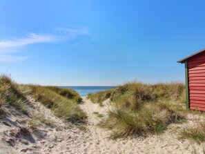 A sandy path leading to a red building, surrounded by grassy dunes.