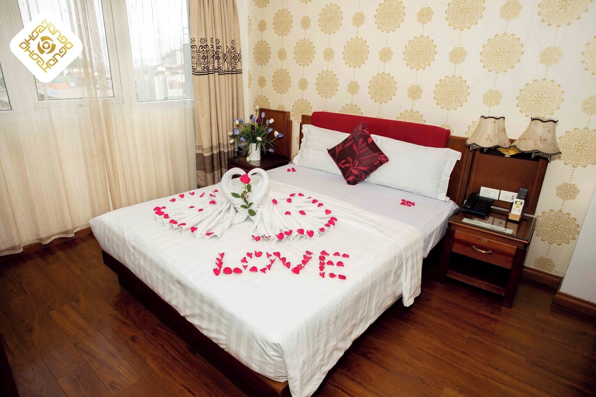 A neatly made bed with a bouquet of flowers and rose petals spelling "LOVE" on the bedspread.