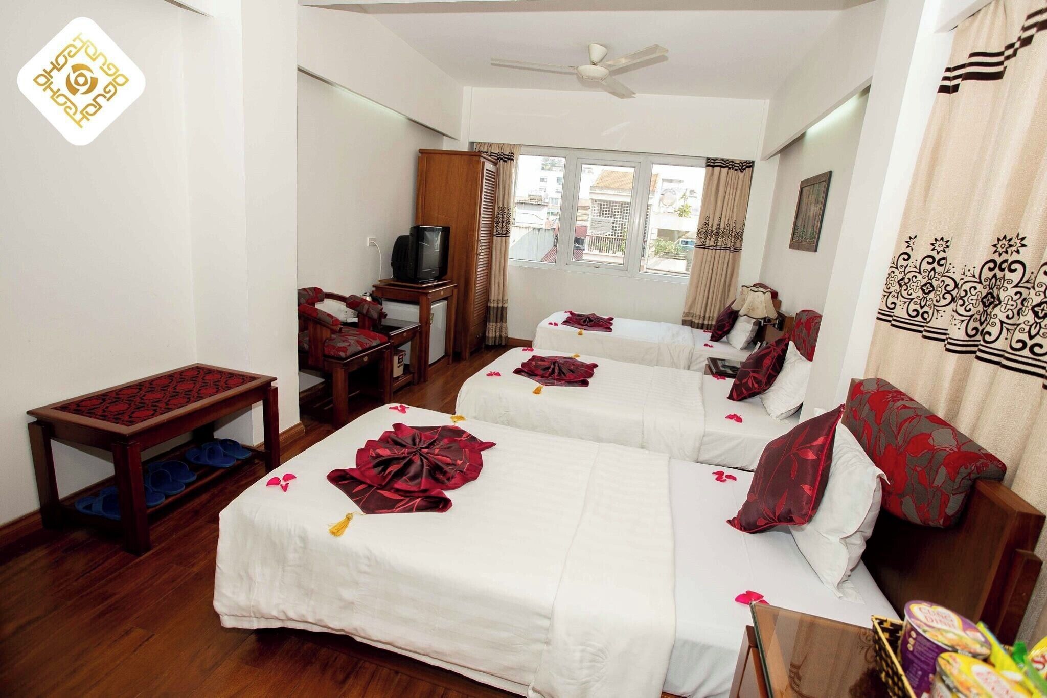 A hotel room with two beds, a television, a small table, and a window with curtains.