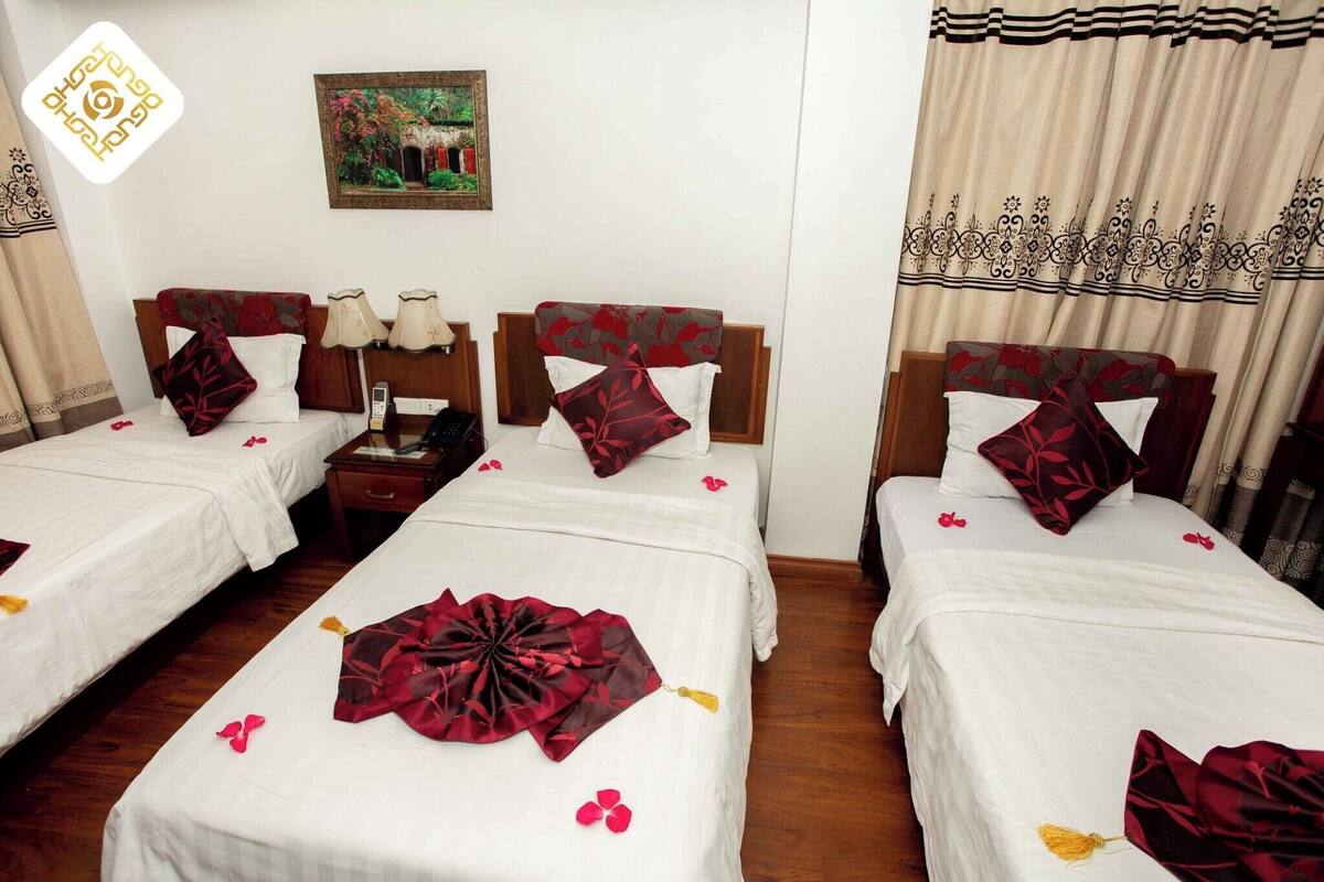 Una habitació d'hotel amb dos llits individuals, cadascun amb una mantella blanca i coixins decoratius vermells. Hi ha una tauleta de nit amb una làmpada i un telèfon entre els llits. Un quadre penja a la paret sobre els llits.