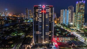 Un hôtel de grande hauteur, surmonté d’un grand panneau lumineux en forme de « rubis », se dressant au milieu d’un paysage urbain nocturne.