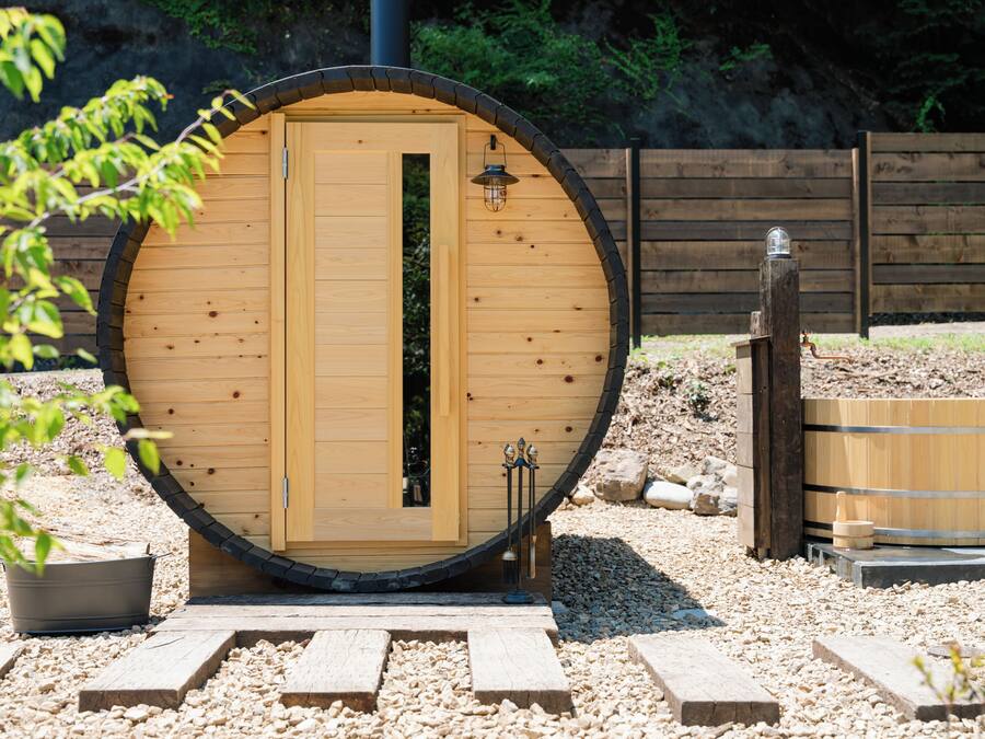 A wooden sauna with a large door and a small window, surrounded by gravel and wooden walkways.