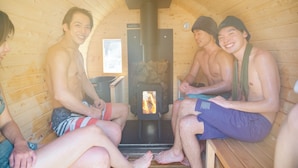A sauna with wooden walls and benches, a visible wood-burning stove, and a small window. - Tsuzuya Village, a guesthouse with a full-fledged private sauna (Minokamo)