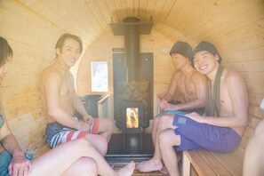A sauna with wooden walls and benches, a visible wood-burning stove, and a small window. - Tsuzuya Village, a guesthouse with a full-fledged private sauna (Minokamo)