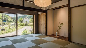 A traditional Japanese room with tatami flooring, a shoji screen door, and a view of greenery outside. - Tsuzuya Village, a guesthouse with a full-fledged private sauna (Minokamo)