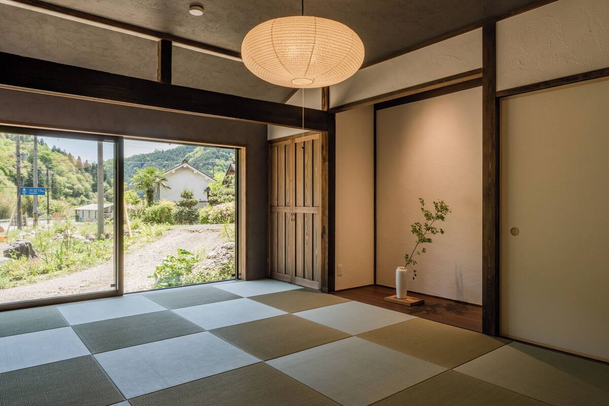 Um quarto japonês tradicional com tatames, um portas de papel shoji e vista para o exterior com vegetação.