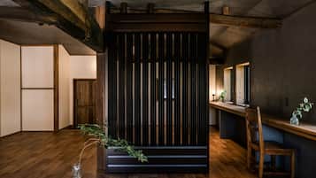 A room with wooden flooring, a sliding door, a wooden chair, a small table with a plant, and a mirror on the wall.